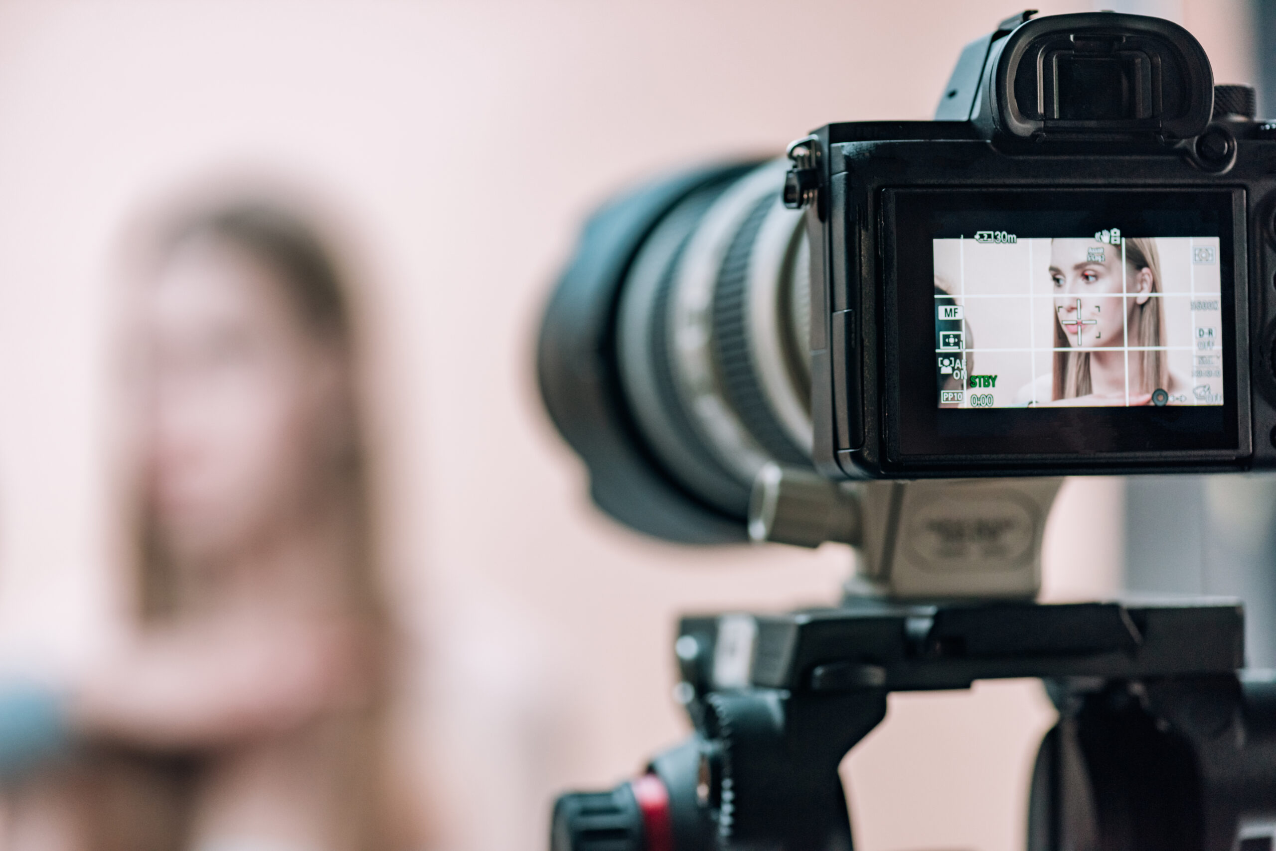 Kamera, die eine Frau im Hintergrund filmt, mit der Frau auf dem Display. Symbolisiert die Integration von passendem Content durch die Chiemsee Filmstudios beim Webdesign.